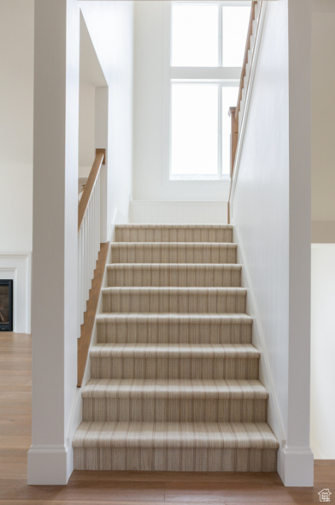 Staircase featuring wood finished floors and a glass covered fireplace