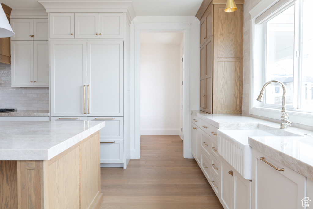 Kitchen with a sink, baseboards, tasteful backsplash, light wood-style floors, and light stone countertops