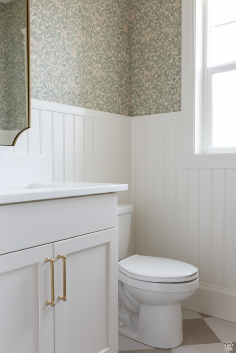 Half bathroom with vanity, a wainscoted wall, toilet, wallpapered walls, and a decorative wall