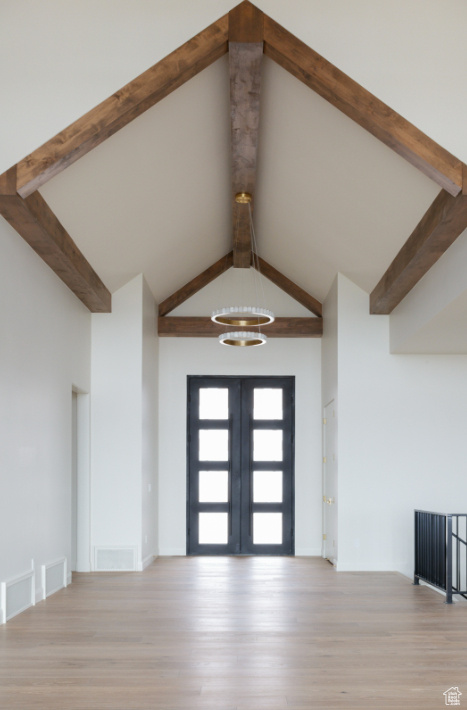 Foyer entrance with beamed ceiling, wood finished floors, high vaulted ceiling, a chandelier, and french doors