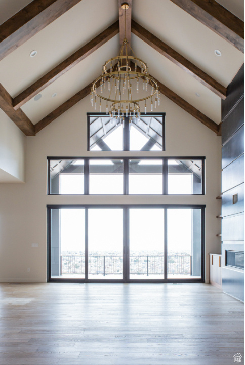 Unfurnished living room featuring a chandelier, high vaulted ceiling, beamed ceiling, wood finished floors, and a glass covered fireplace