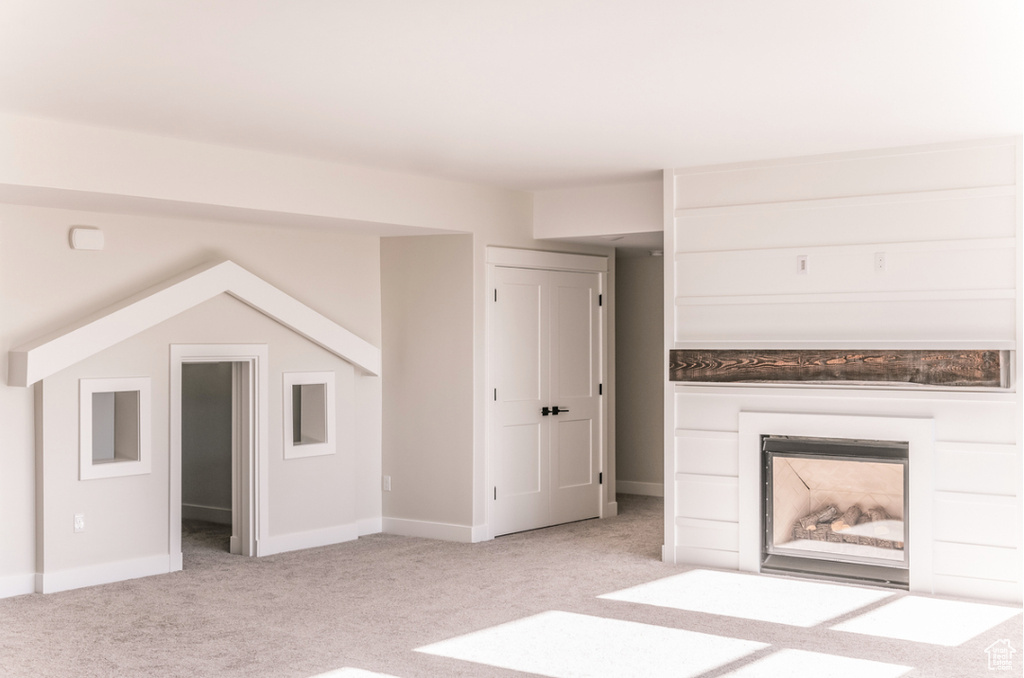 Unfurnished living room with light carpet, a glass covered fireplace, and baseboards