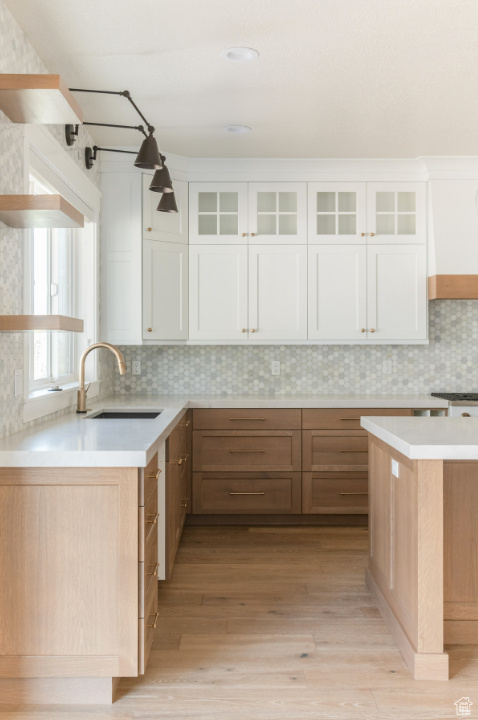 Kitchen with a sink, light wood-type flooring, tasteful backsplash, white cabinetry, and light countertops