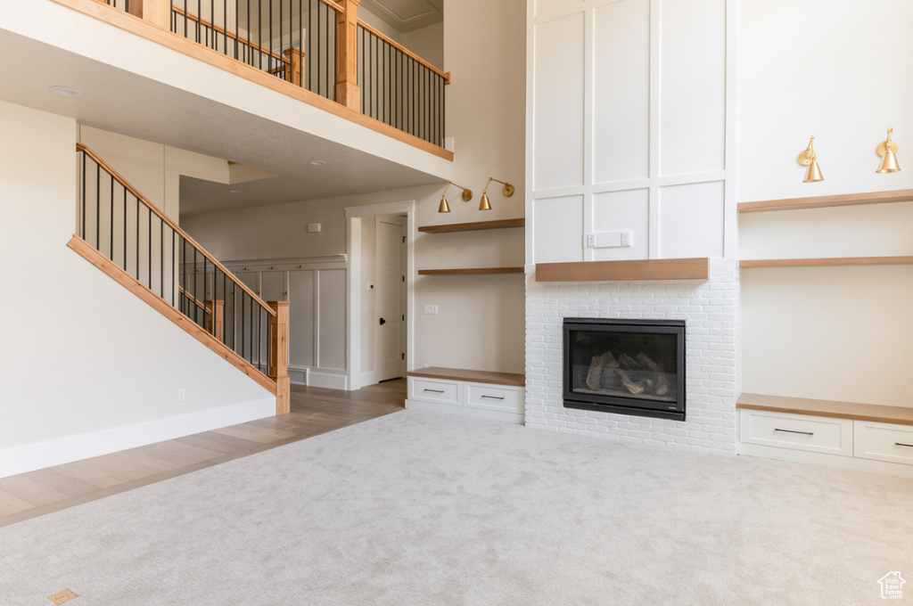Unfurnished living room featuring carpet, a towering ceiling, stairway, and a fireplace