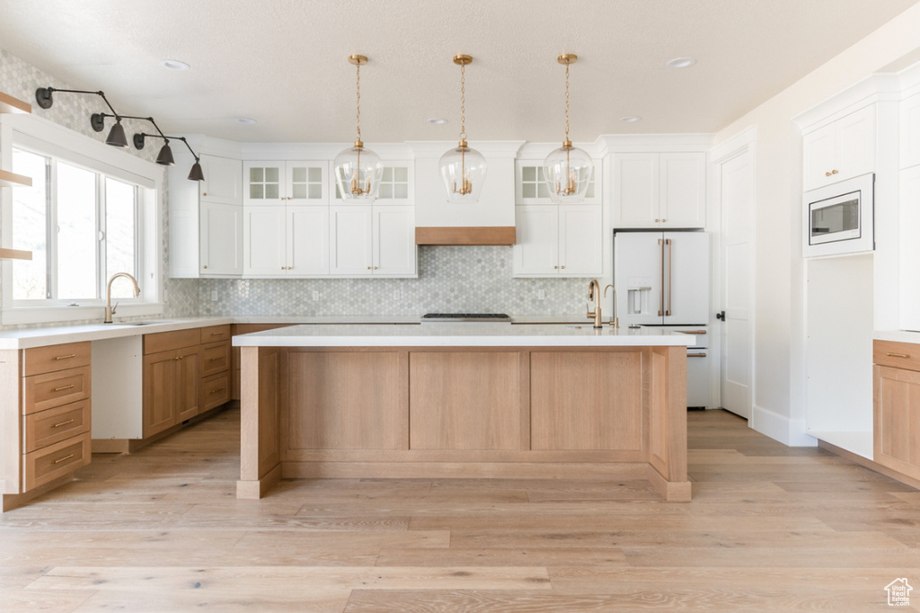 Kitchen featuring high end fridge, a sink, decorative backsplash, light wood finished floors, and recessed lighting