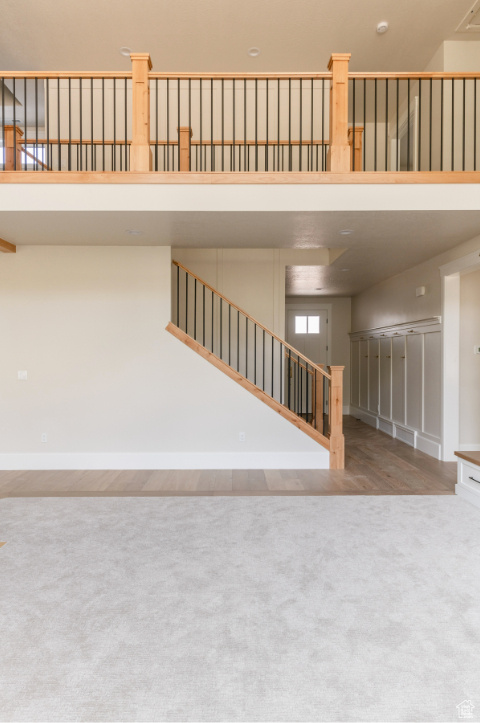 Unfurnished living room with carpet, stairway, a towering ceiling, and baseboards