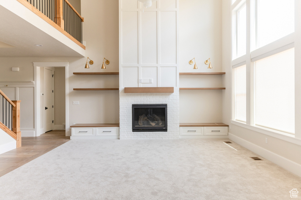 Unfurnished living room featuring carpet floors, a brick fireplace, stairway, a high ceiling, and baseboards