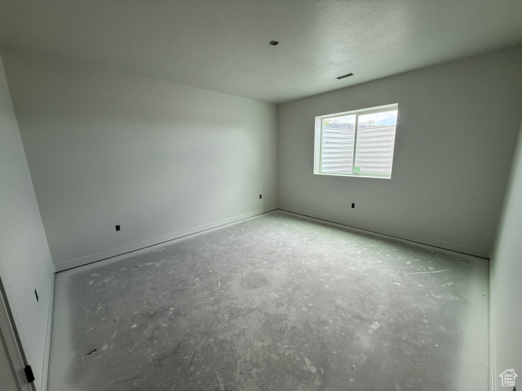 Empty room featuring a textured ceiling, concrete flooring, and baseboards