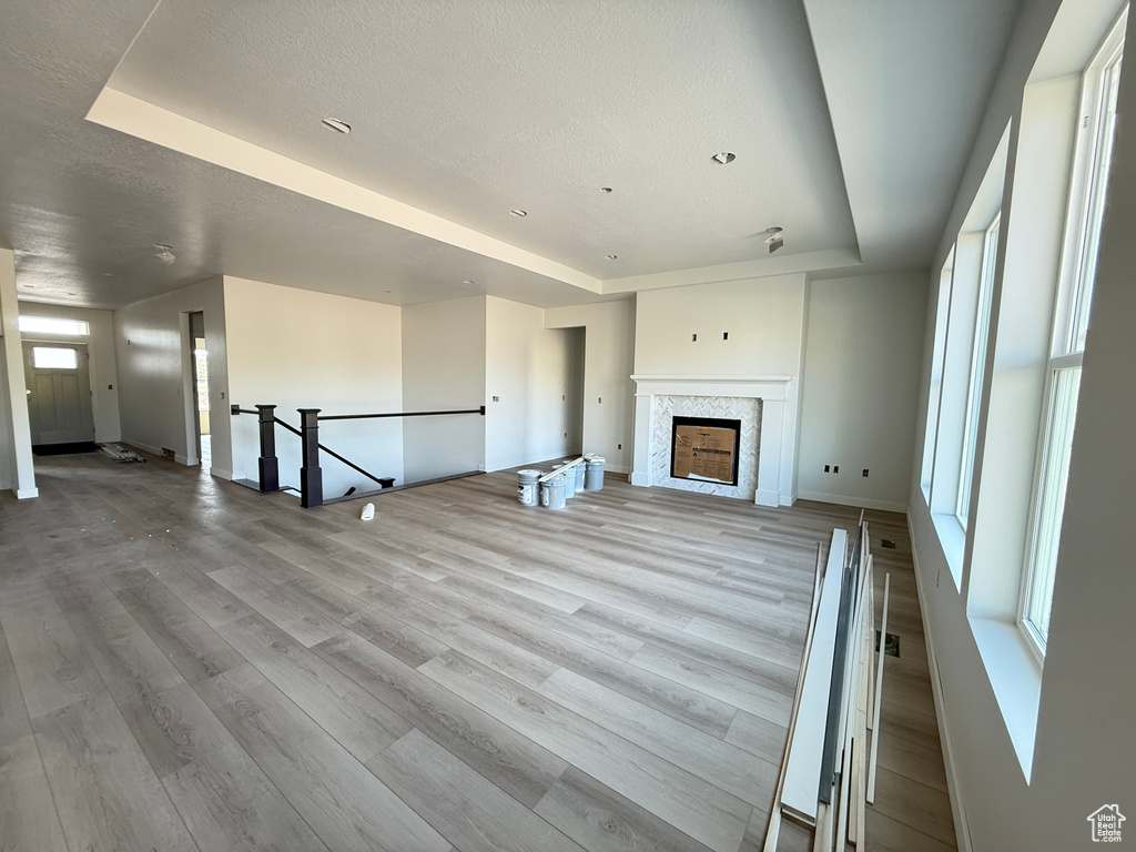 Unfurnished living room with a tray ceiling, baseboards, wood finished floors, and a fireplace