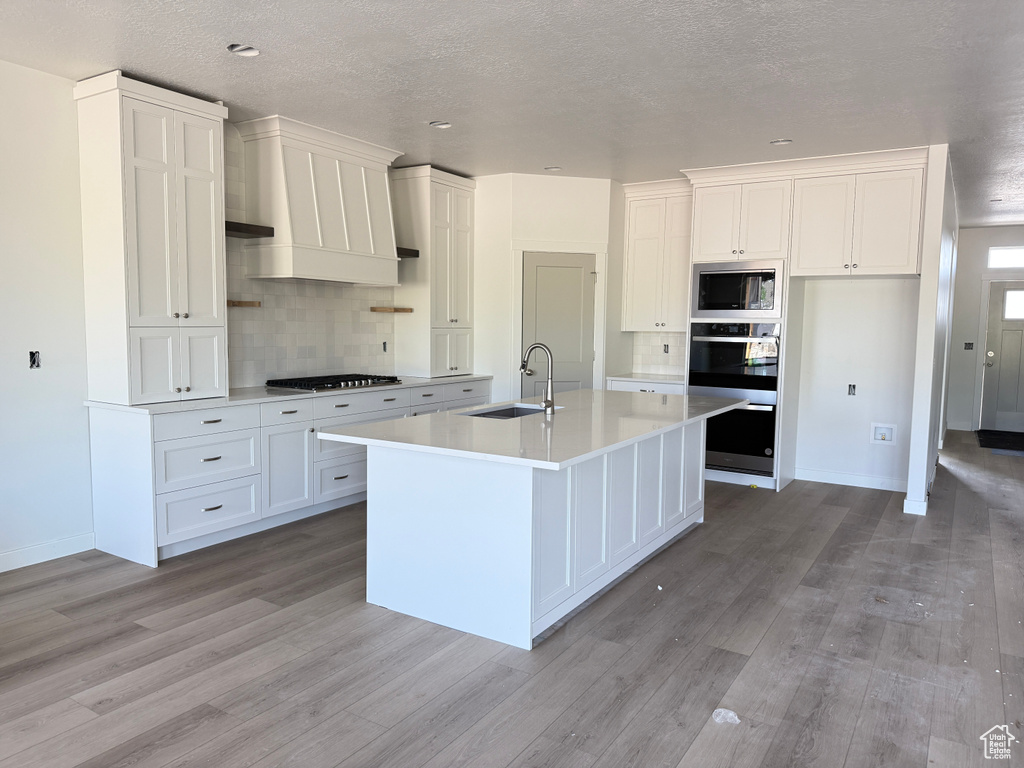 Kitchen with a sink, appliances with stainless steel finishes, decorative backsplash, light wood finished floors, and a textured ceiling