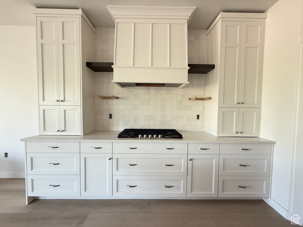Kitchen featuring stainless steel gas stovetop, backsplash, white cabinets, and light countertops