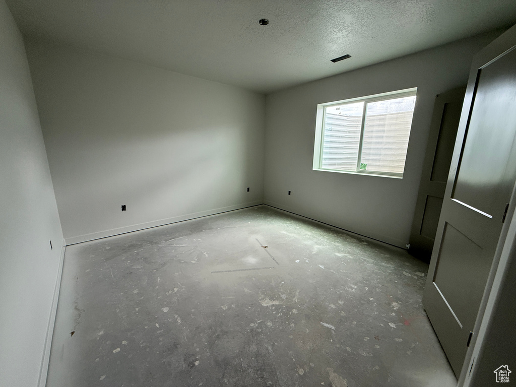 Empty room featuring a textured ceiling, unfinished concrete flooring, and baseboards