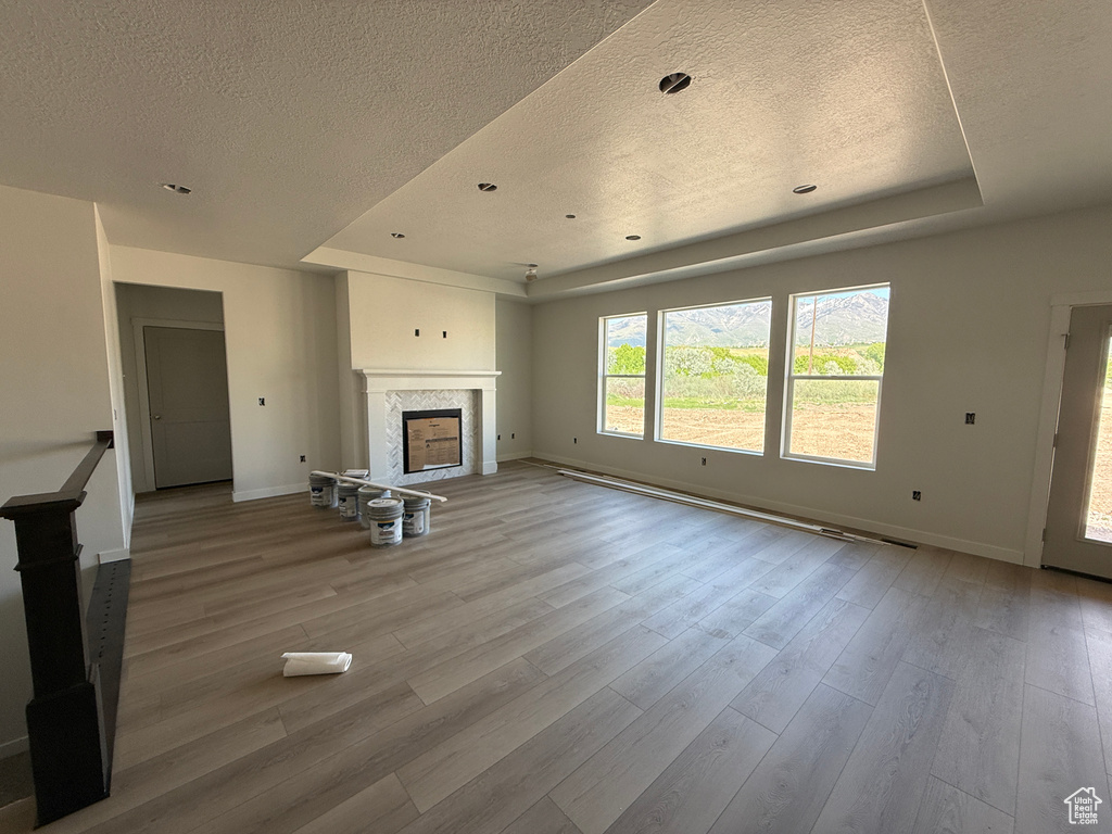Unfurnished living room featuring a textured ceiling, a raised ceiling, baseboards, a fireplace, and wood finished floors