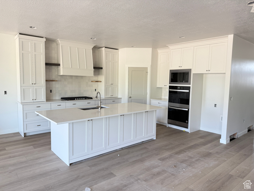 Kitchen with a sink, gas stovetop, light wood-style floors, tasteful backsplash, and a textured ceiling