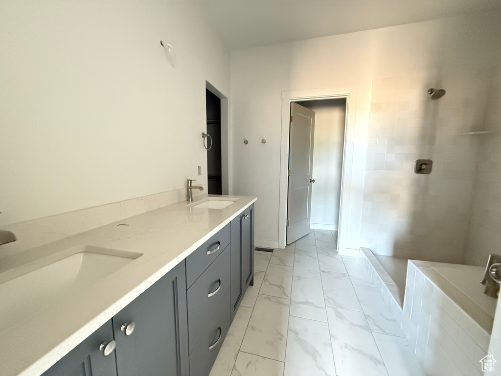 Bathroom with marble look tiles, a tile shower, and double vanity