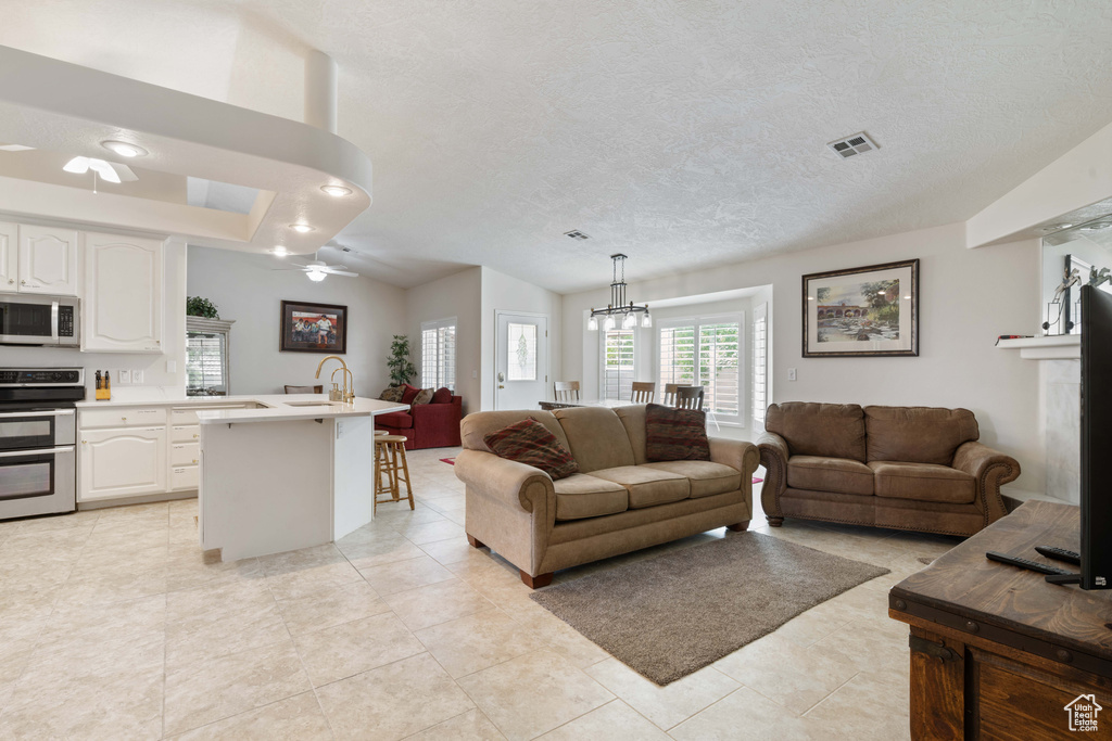 Living area with a ceiling fan, a chandelier, light tile patterned floors, and a textured ceiling