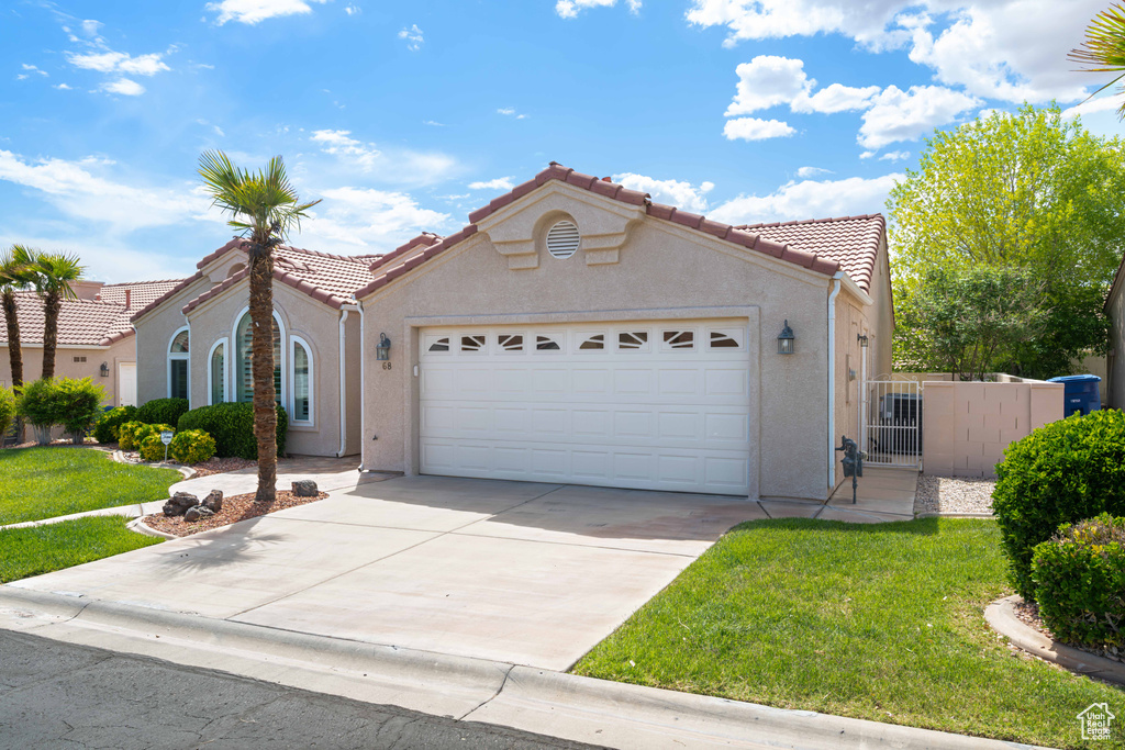 Mediterranean / spanish-style home featuring a tiled roof, an attached garage, driveway, stucco siding, and a gate