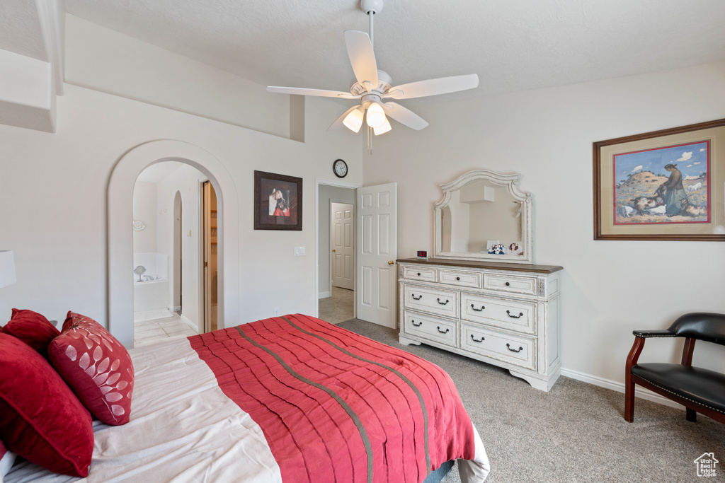 Bedroom with arched walkways, baseboards, carpet flooring, a ceiling fan, and connected bathroom