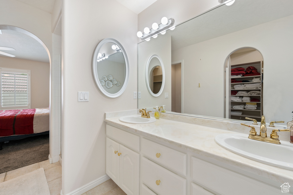 Ensuite bathroom with tile patterned flooring, double vanity, a walk in closet, and baseboards