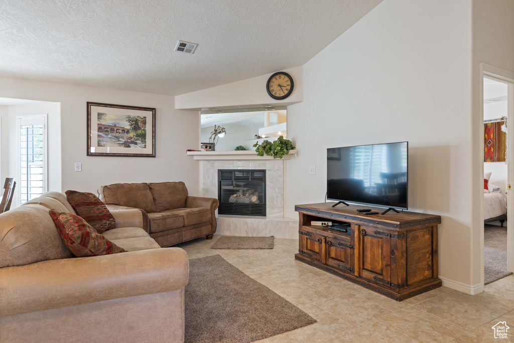 Living area featuring a high end fireplace, light tile patterned flooring, a textured ceiling, and vaulted ceiling