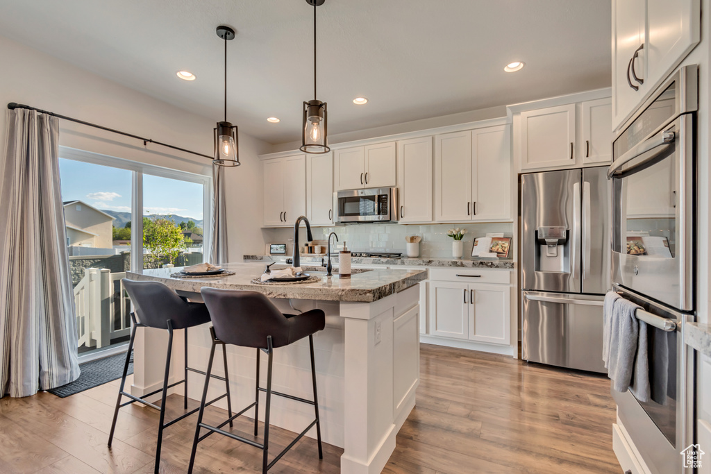 Kitchen with stainless steel appliances, recessed lighting, white cabinets, light stone countertops, and a kitchen island with sink
