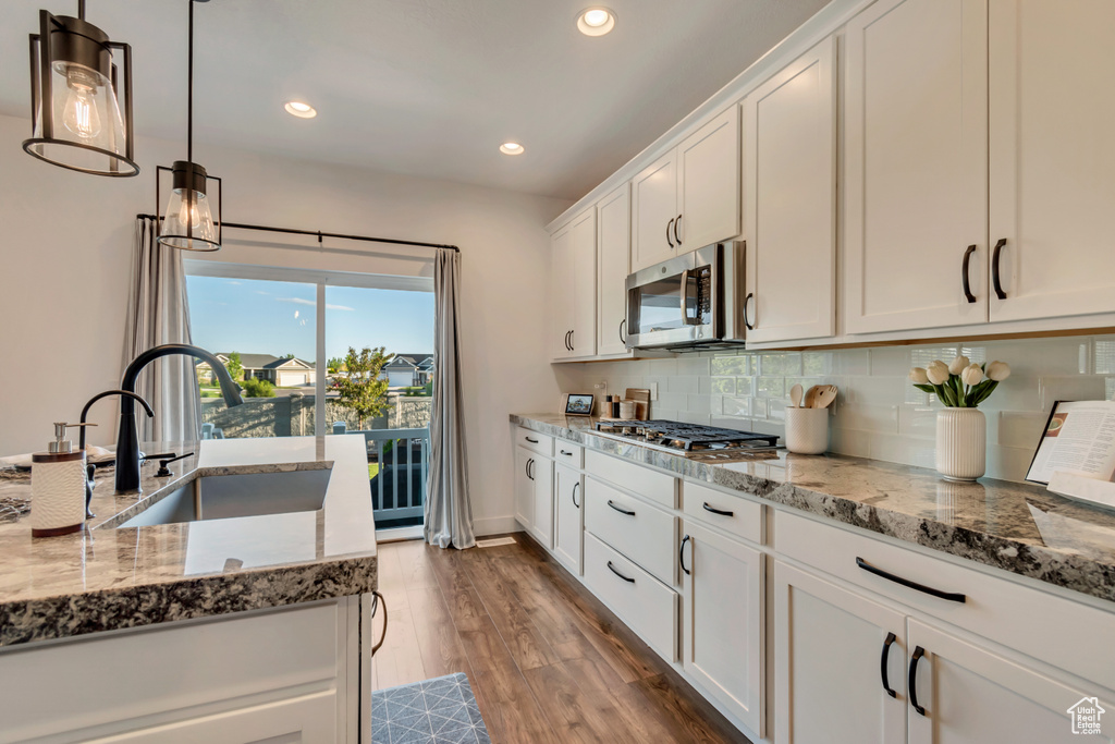 Kitchen featuring appliances with stainless steel finishes, a sink, white cabinetry, decorative backsplash, and light stone countertops