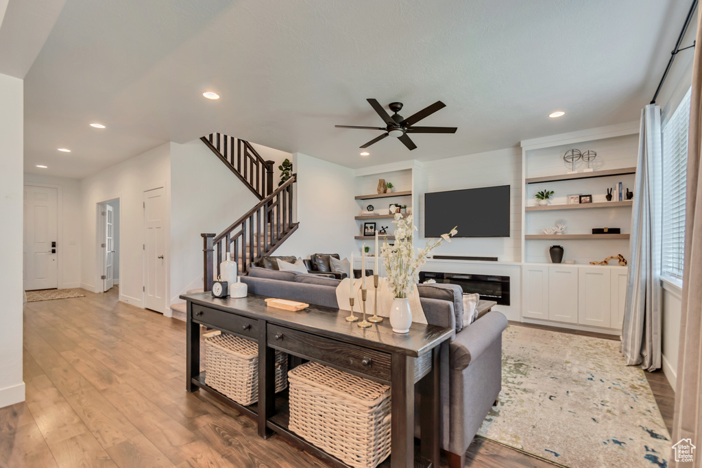 Living room featuring ceiling fan, stairs, recessed lighting, wood finished floors, and a glass covered fireplace