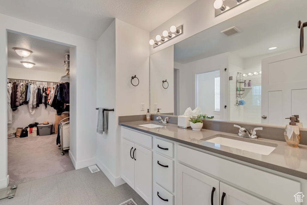 Bathroom with a tile shower, a spacious closet, double vanity, and baseboards