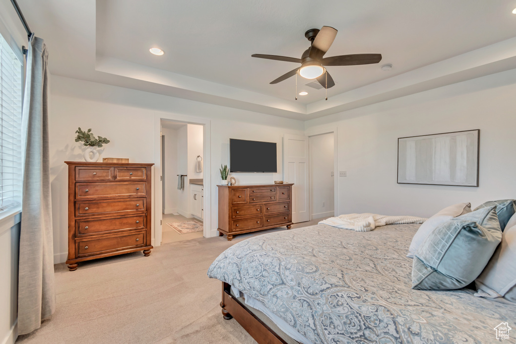 Bedroom featuring a raised ceiling, light colored carpet, recessed lighting, multiple windows, and ensuite bath