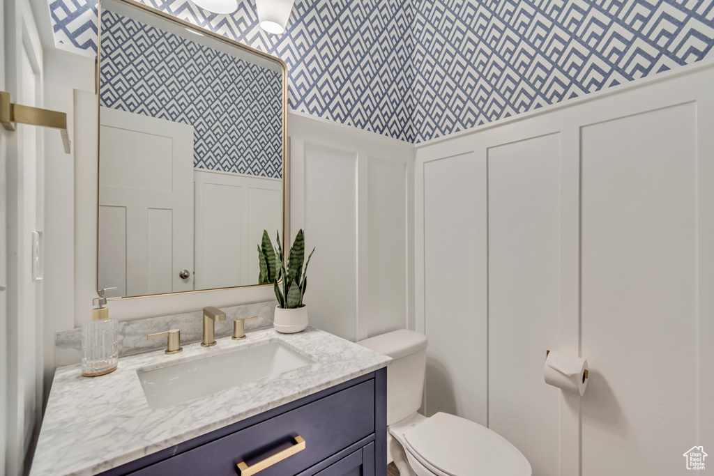 Bathroom featuring a decorative wall, wallpapered walls, toilet, vanity, and a wainscoted wall