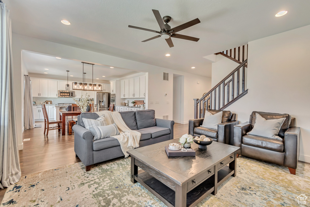 Living room with a ceiling fan, recessed lighting, light wood-style flooring, and stairs