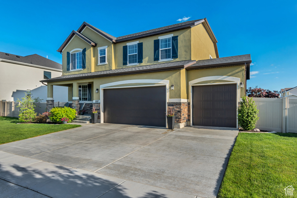 View of front of house with stucco siding, driveway, stone siding, and an attached garage