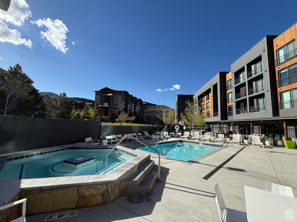 Community pool with a hot tub, fence, and a patio