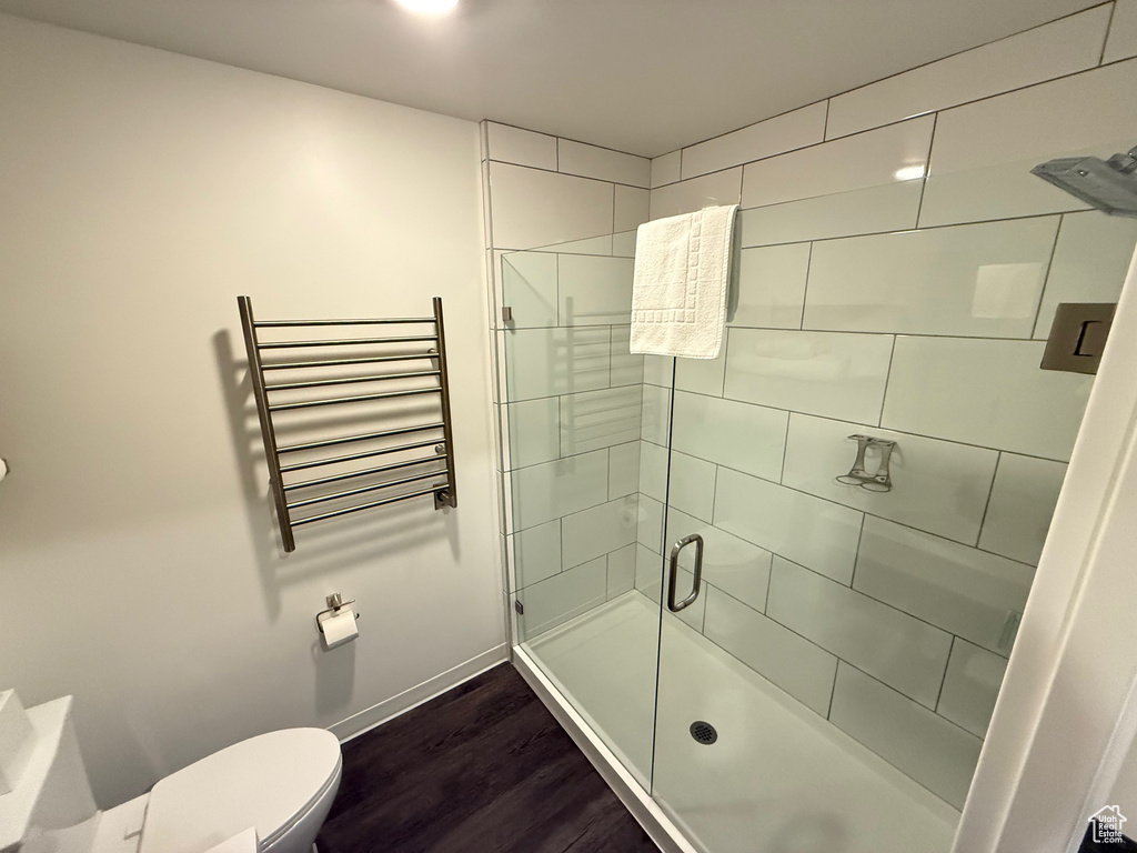 Full bath with radiator, toilet, wood finished floors, a stall shower, and baseboards