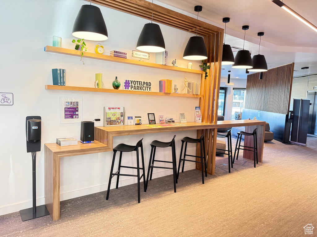 Bar with carpet flooring, baseboards, and hanging light fixtures