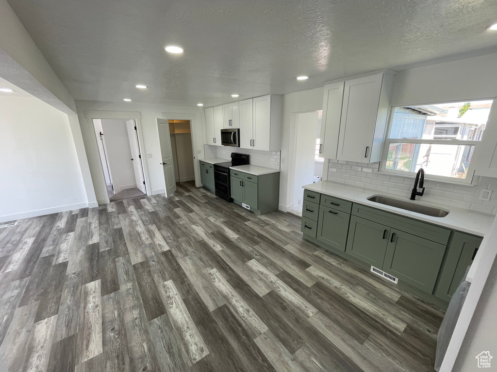 Kitchen with a sink, double oven range, stainless steel microwave, green cabinets, and wood finished floors