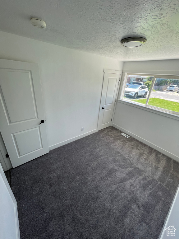 Empty room with dark colored carpet, a smoke detector, baseboards, and a textured ceiling