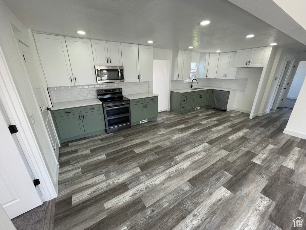 Kitchen with appliances with stainless steel finishes, green cabinets, a sink, dark wood finished floors, and backsplash