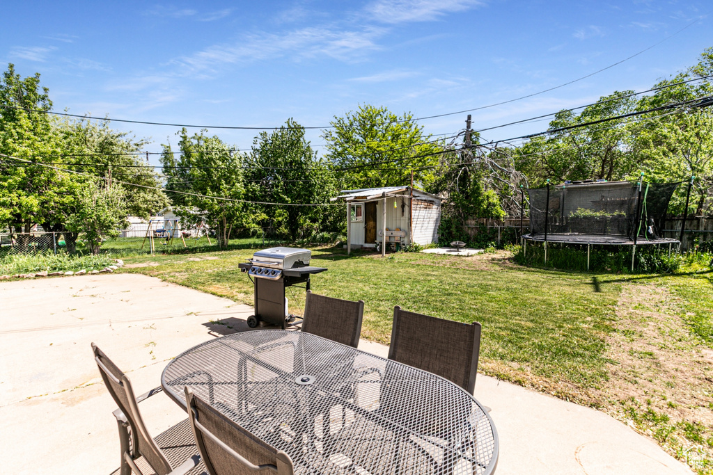 View of patio featuring a trampoline, a grill, outdoor dining area, a storage unit, and an outbuilding