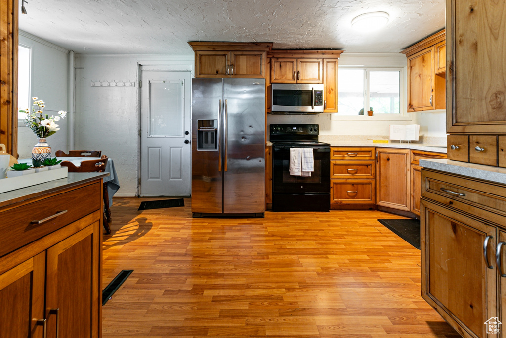 Kitchen with stainless steel appliances, light wood-style floors, a textured ceiling, brown cabinetry, and light countertops