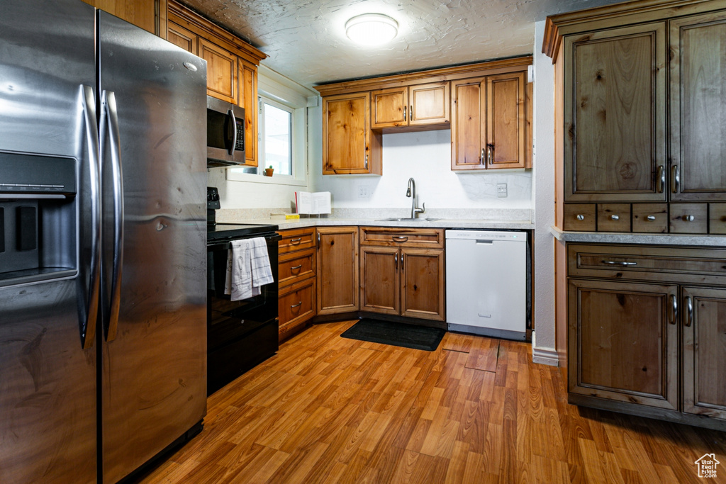 Kitchen featuring stainless steel appliances, a sink, wood finished floors, brown cabinets, and light countertops