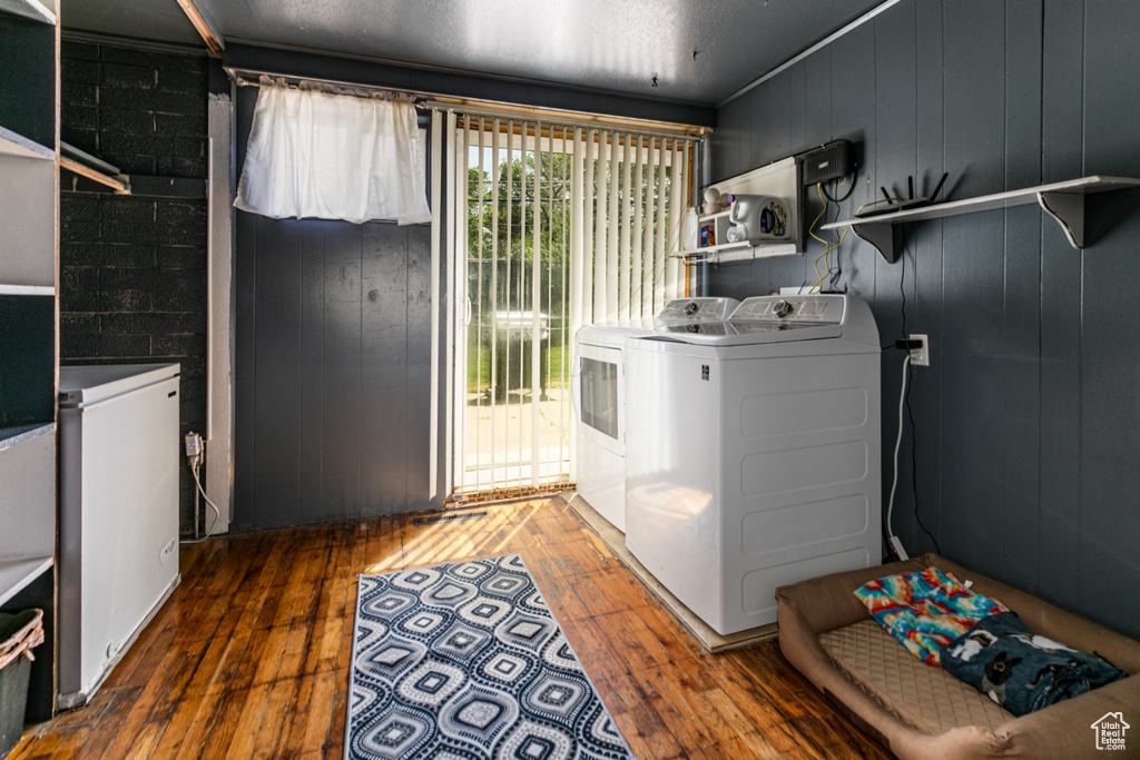 Laundry room with wood-type flooring, washing machine and clothes dryer, and wooden walls