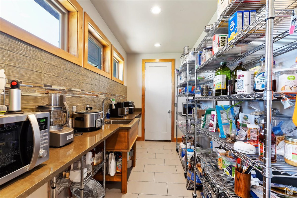 Kitchen featuring a sink, stainless steel microwave, backsplash, recessed lighting, and tile patterned flooring
