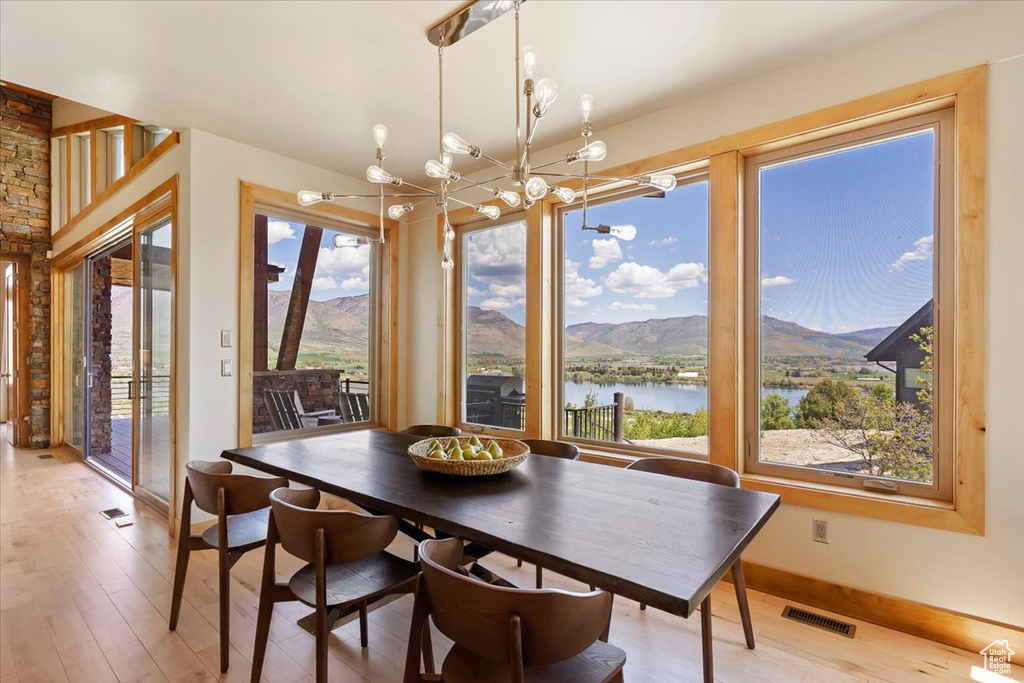 Dining room featuring a chandelier, light wood-style floors, a water and mountain view, and baseboards