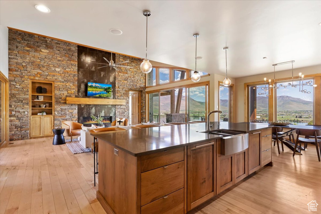 Kitchen featuring a sink, dark countertops, a stone fireplace, light wood finished floors, and a kitchen island with sink