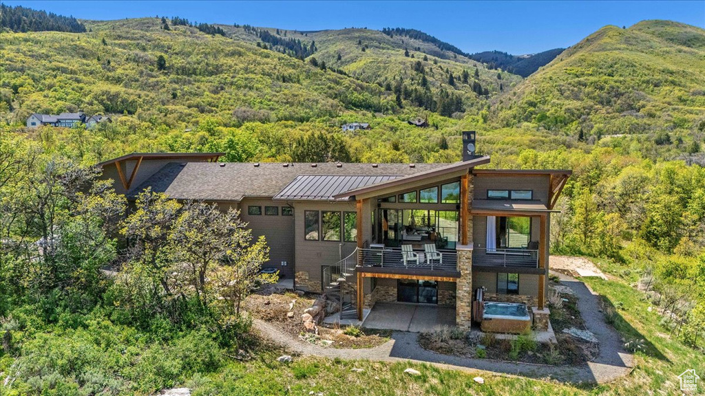 Back of property featuring a patio area, a standing seam roof, stone siding, a forest view, and a deck with mountain view