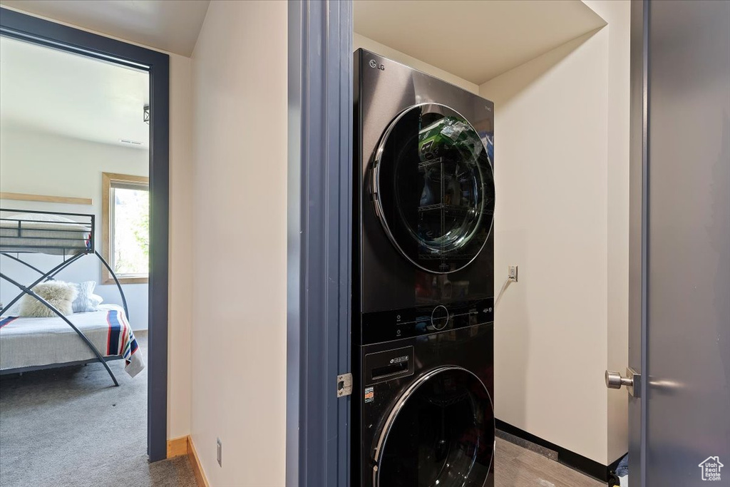 Clothes washing area with stacked washing machine and dryer, baseboards, and carpet