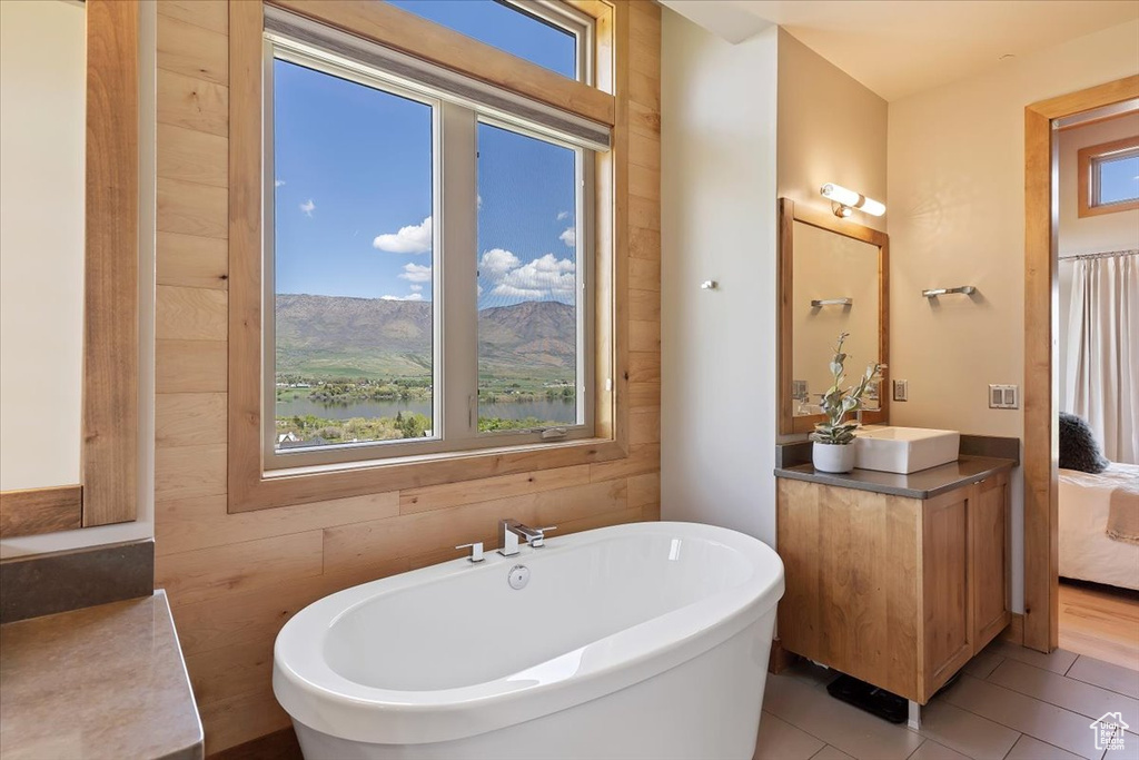 Ensuite bathroom featuring healthy amount of natural light, a soaking tub, vanity, and tile patterned floors