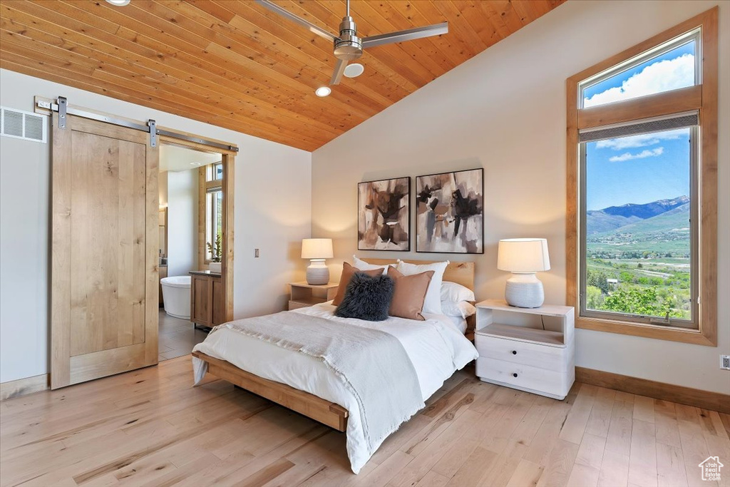 Bedroom with multiple windows, vaulted ceiling, baseboards, a barn door, and hardwood / wood-style flooring