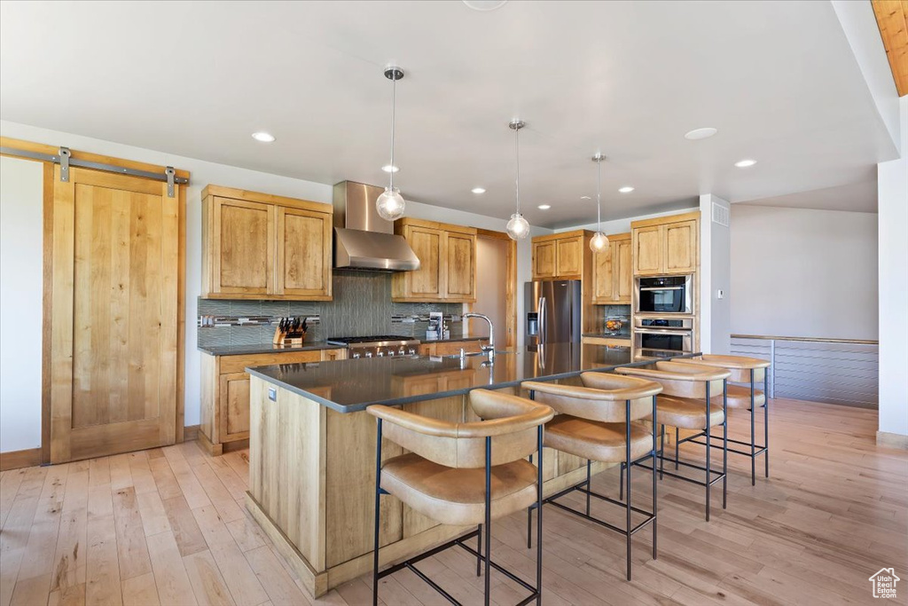 Kitchen with stainless steel appliances, dark countertops, a spacious island, light wood finished floors, and recessed lighting